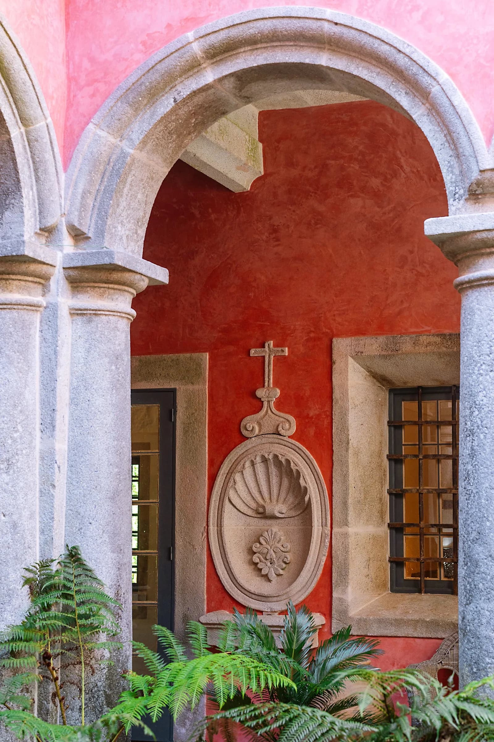 The red cloister arch with stone columns and ferns