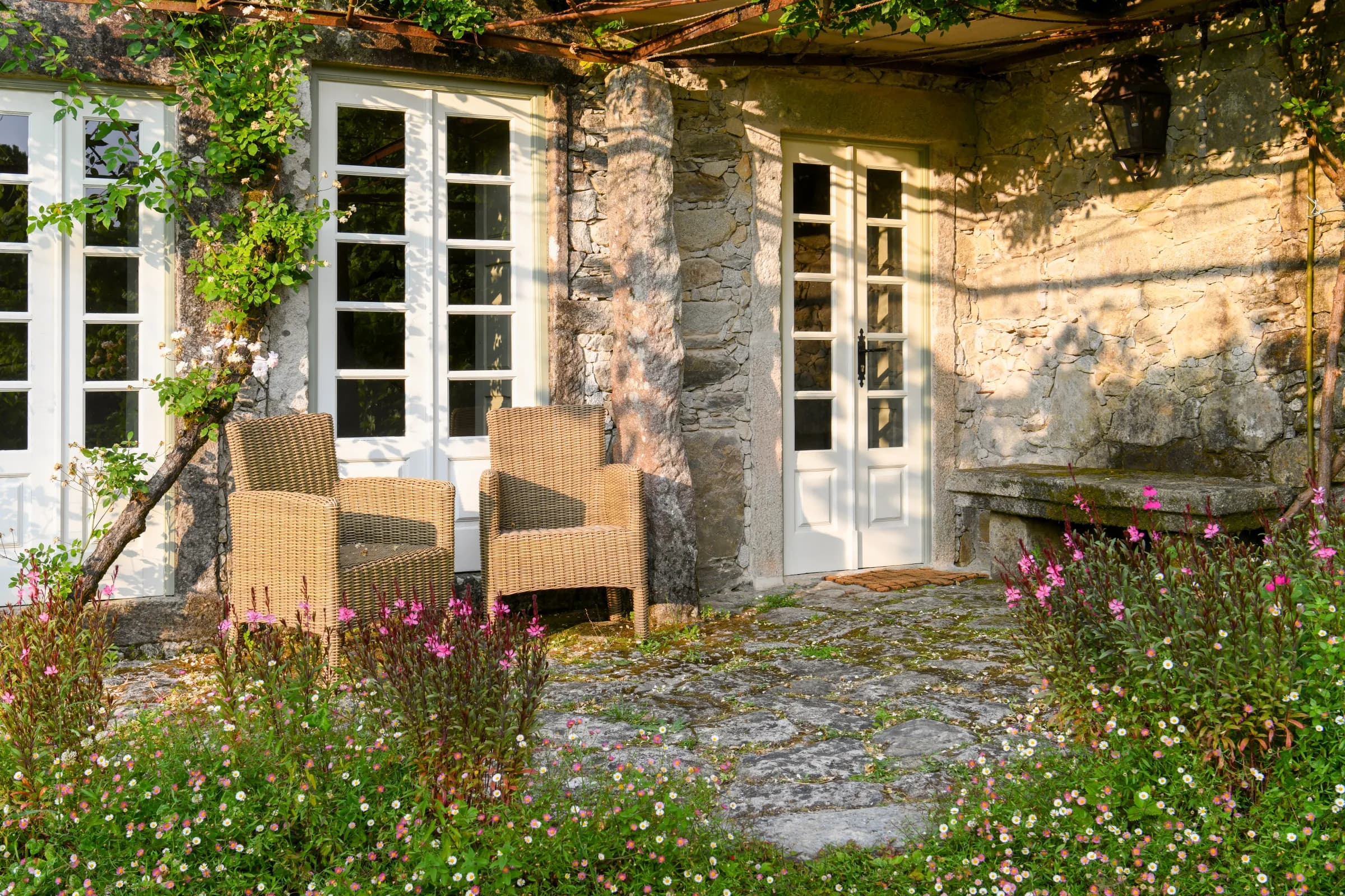 The stone pergola terrace, wicker chairs among wildflowers