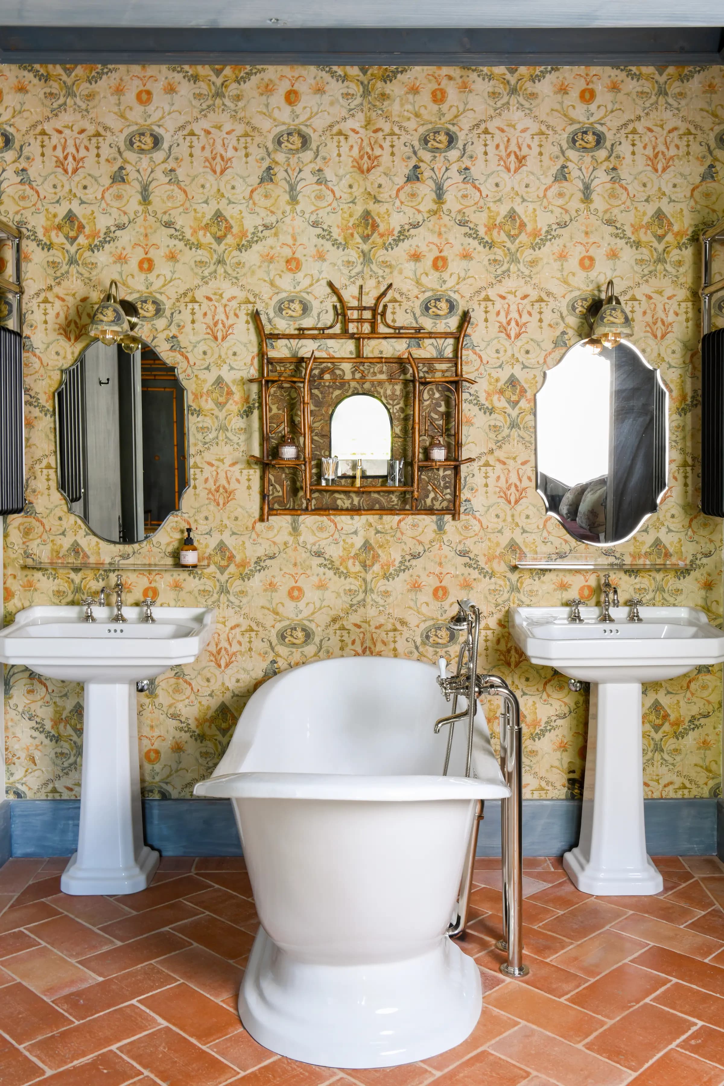 A freestanding bathtub between two basins, on terracotta tiles