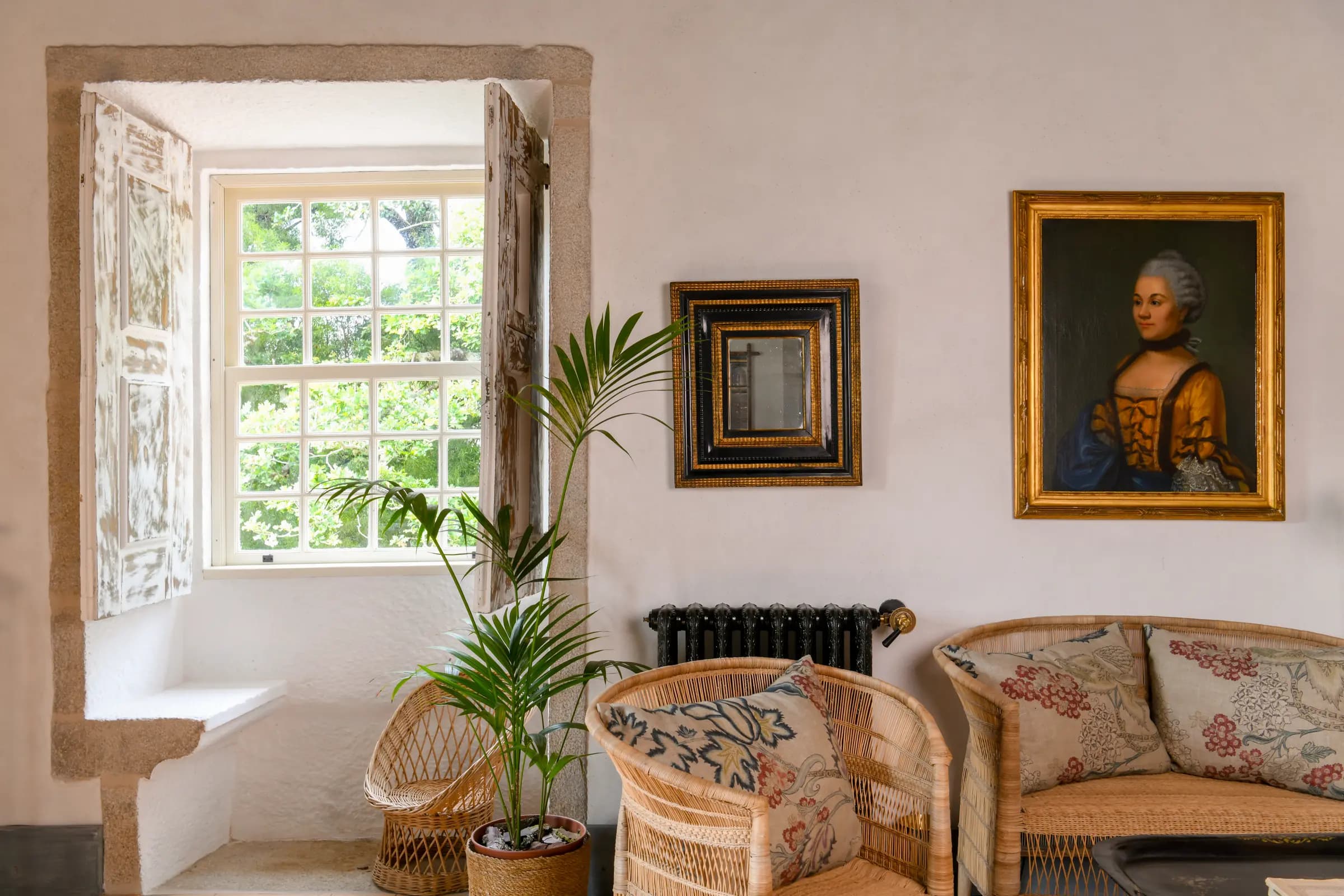 A deep stone window seat beside rattan chairs and an old portrait
