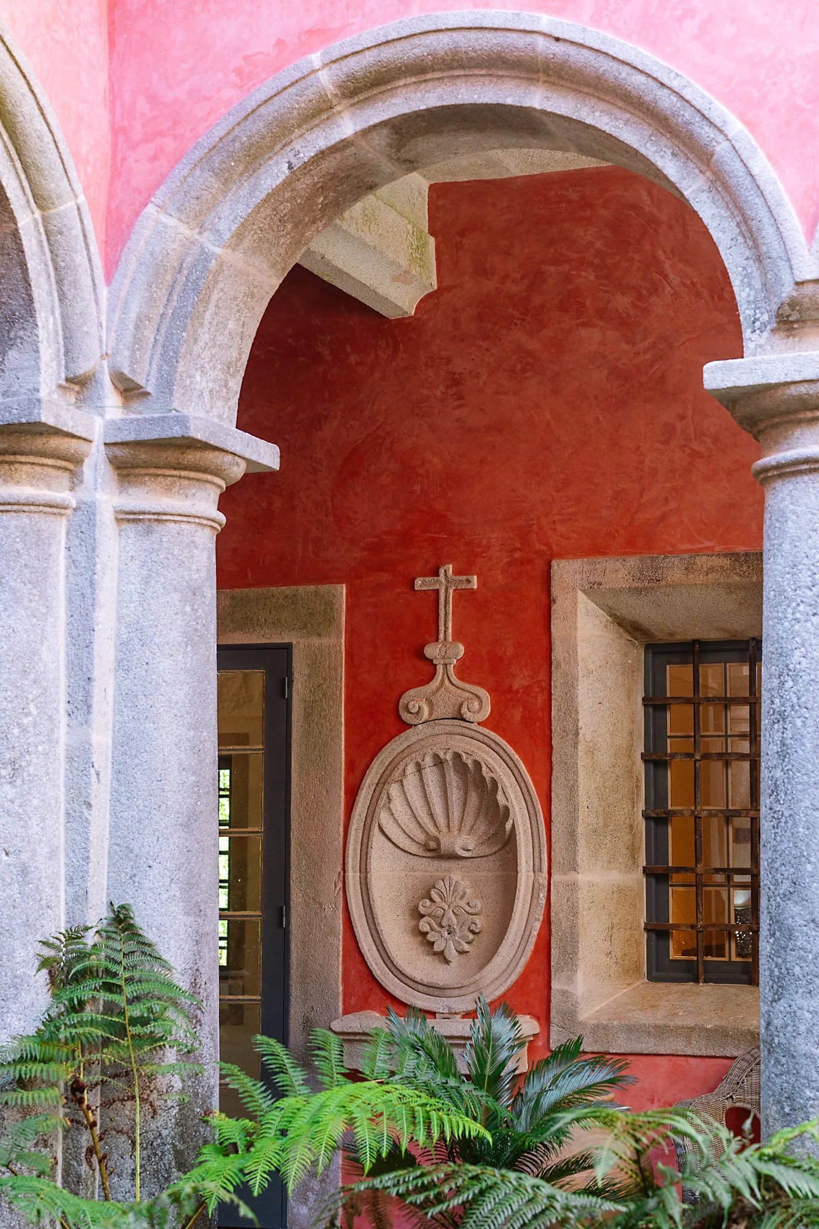 The red cloister arch with old stone columns and ferns